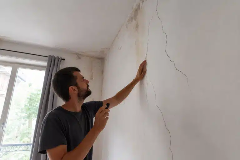 Homme examinant fissures murales près du plafond